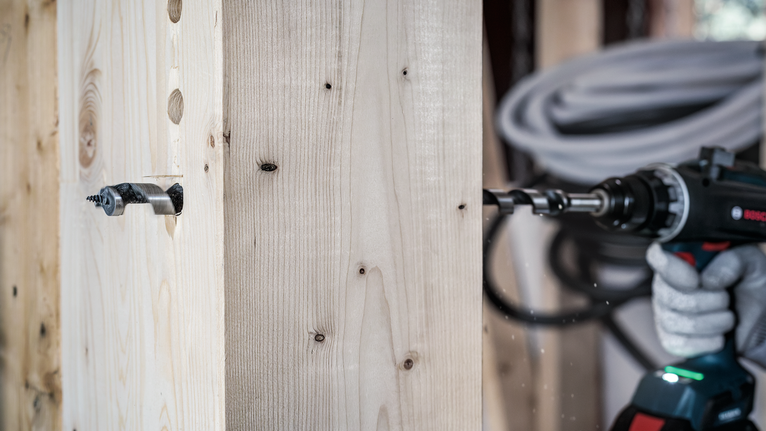 PRO Wood Auger Bit, 10 x 385 x 450 mm Worker wearing safety equipment drills a large screw into thick wooden beams.