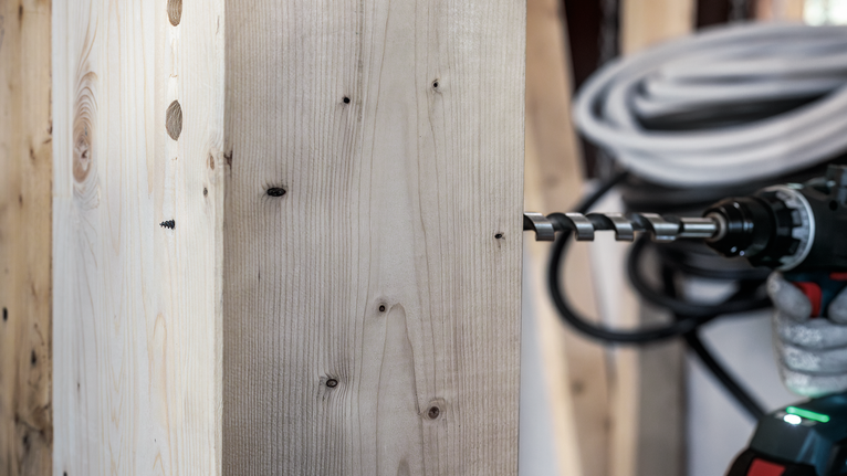 PRO Wood Auger Bit, 10 x 385 x 450 mm Person wearing safety equipment drills through thick wooden board.