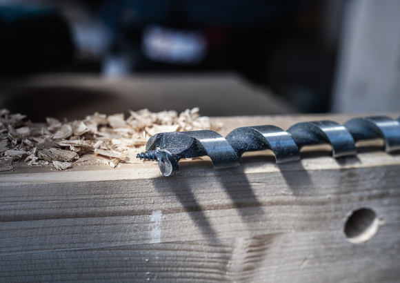 Object #200479960: 3088579_app_web_009 Wood drill bit resting on a plank with fresh wood shavings nearby.